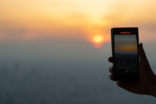 Close-up of persons hand photographing sunset through smart phone