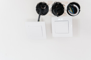 two white electric light switches with exposed wires on unfinished wall