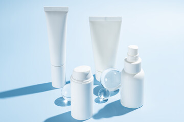 Mockup of white plastic bottles and tubes with face serum or cream, or toner on blue background with glass balls. The concept of beauty cosmetics, natural products for moisturizing and restoring skin.