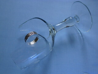 a broken wine glass lying on a blue surface with a silver ring hanging on a sharp glass shard. The image symbolizes relationship breakdown.