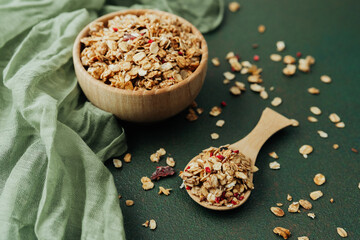 Wooden bowl and scoop of granola on green textile background
