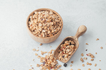 Granola in wooden bowl and scoop on light gray background