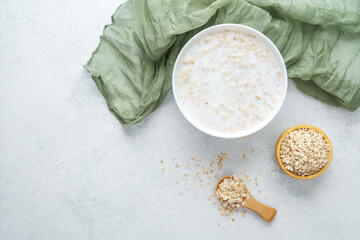 Oatmeal porridge in white bowl with oats and green fabric