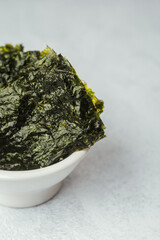 Crispy roasted nori seaweed snack on wooden board and ceramic bowl with white and green background