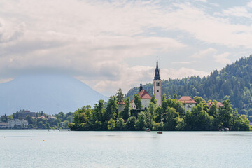 Bled Island with church in calm lake and scenic alpine background.