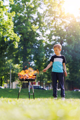 Cute little adorable baby boy put wooden stick in fire pit with huge fire at city park or house yard. Child play dangerous game with bonfire. Fire accident risk and health damage concept