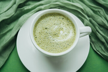 Macro shot of foamy matcha latte in white cup on green table