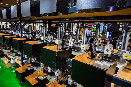 Multiple 3D printers operate simultaneously on shelves in a factory or production facility, showcasing modern manufacturing technology and automation on a large scale.