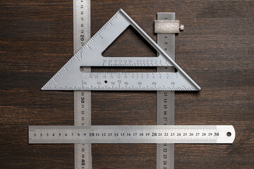 Measuring tool, metal rulers, triangle on wooden background in shape of house, closeup, top view. Concept of measuring, construction and repair
