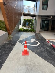 Editorial: Krabi, Thailand. June 2025. A designated accessible parking space, marked with a clear wheelchair symbol on the ground and a traffic cone. Signage in the background indicates a "Handicapped