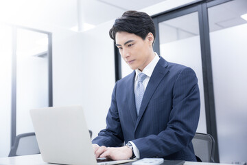 会議室でパソコンの仕事をするスーツを着た男性