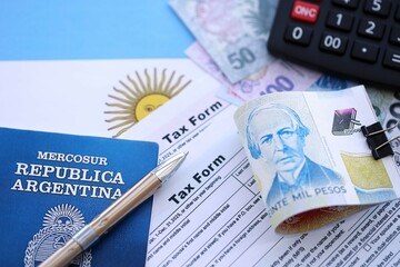 Argentine pesos money bills in big amount lies on table with pen, calculator, passport and tax forms