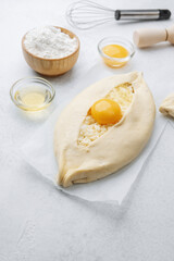 Uncooked khachapuri with egg yolk and whisk on white background