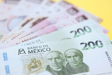 Mexican pesos money bills in big amount lies on yellow color table close up