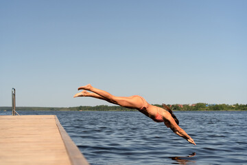 Athletic woman in swimsuit diving headfirst from a pier into the lake. Sunny summer day, dynamic outdoor action.