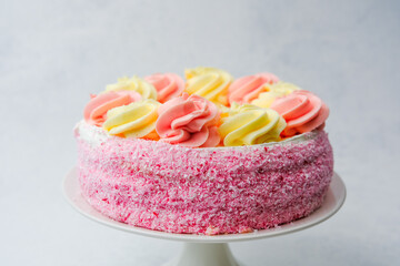 Pink and yellow frosted cake decorated with cream swirls on a stand