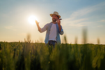 Farmer wearing a straw hat gesturing with one hand while talking on a mobile phone in a golden...