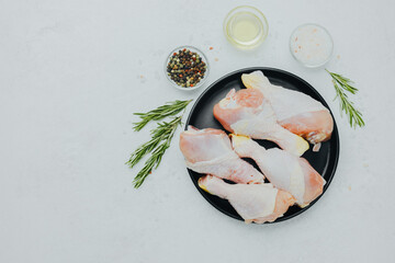 Raw chicken drumsticks on black plate with rosemary and spices