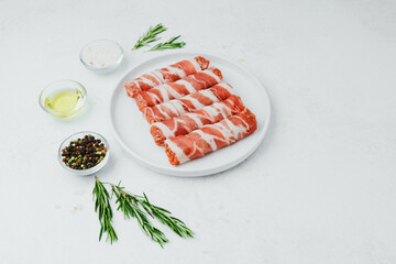 Bacon wrapped sausage rolls on white plate with herbs and oil