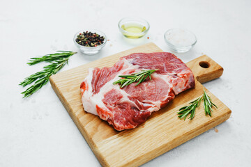 Fresh pork steak with rosemary on wooden cutting board
