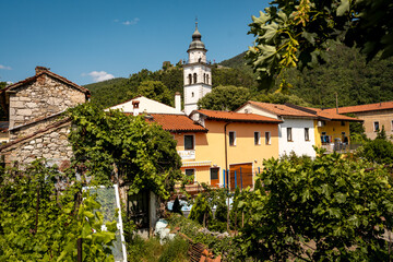 Charming Townscape Of Vipava With Castle View: Colorful Historic Houses And Church Tower Nestled Below Forested Hills With Distant Castle Ruins Under A Clear Blue Sky In Western Slovenia