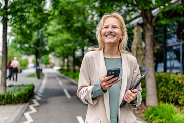 Young woman with albinism smiles while holding a phone and tablet on a sunny day in an urban park