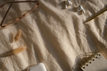 Glasses, wireless earbuds, pen, notebook, and dried grasses on fabric, soft light