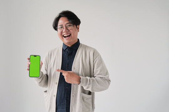 A man is holding a green phone and pointing to it. He is smiling. The phone is green and has a green screen