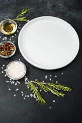 Empty white plate with herbs and spices on black stone background