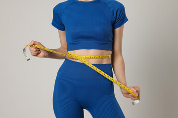 Woman measuring her belly with tape on gray background, closeup