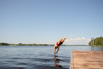 Man diving headfirst from pier into the lake. Strong form, clear water, summer moment.