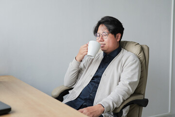 A man is sitting in a chair and drinking from a white cup