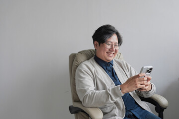 A man is sitting in a chair and looking at his cell phone