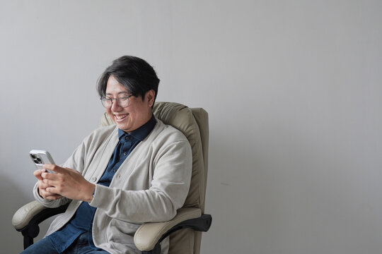 A man is sitting in a chair and looking at his cell phone