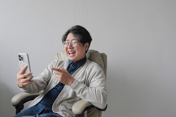 A man is sitting in a chair and pointing at his cell phone