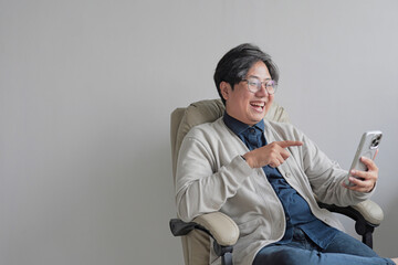 A man is sitting in a chair and pointing at his cell phone