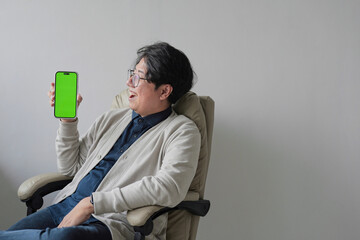 A man is sitting in a chair holding a green iPhone