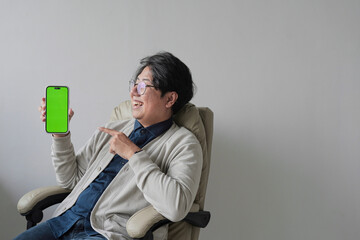 A man is sitting in a chair holding a green phone