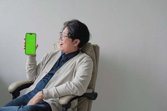 A man is sitting in a chair holding a green iPhone