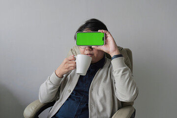 A man is sitting in a chair with a green screen on his phone