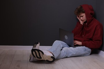 Cyber bullying. Upset teenage boy with laptop on floor indoors. Space for text