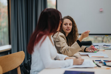 Two women are engaged in a lively discussion at a school or educational setting, illustrating communication and learning. The image captures a moment of interaction and exchange of ideas.