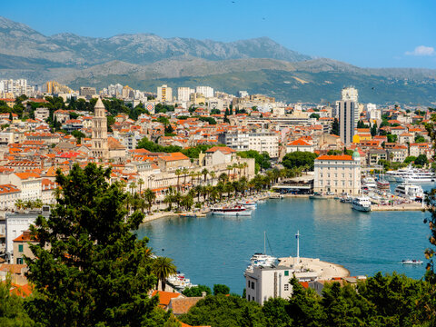 Panoramic view of Split, Croatia from Marjan Hill, featuring the historic old town, bustling harbor, and distant mountains beneath a vibrant blue sky.