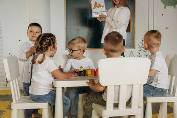 Playing the game by table. Children in kindergarten with their teacher