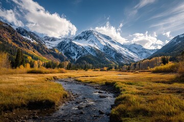 Serene autumn landscape.  A tranquil stream flows through a golden meadow, nestled against majestic snow-capped mountains. Ideal for travel, nature, and environmental projects.