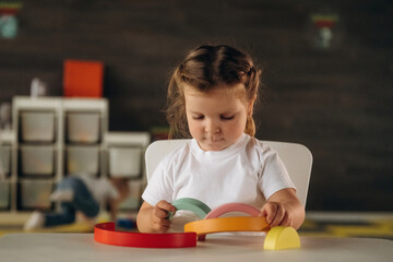 Girl is sitting and playing with toy. Group of children are in the kindergarten