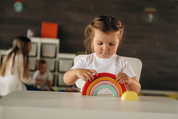 Girl is sitting and playing with toy. Group of children are in the kindergarten