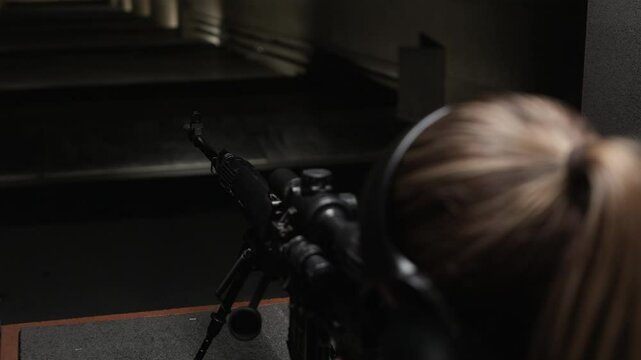 Handheld shot of female trainee in earmuffs pointing and shooting rifle during practice in range