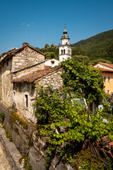 Fototapeta premium Charming Townscape Of Vipava With Castle View: Colorful Historic Houses And Church Tower Nestled Below Forested Hills With Distant Castle Ruins Under A Clear Blue Sky In Western Slovenia