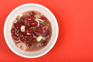 A white bowl holds a vibrant bean and onion salad in a reddish broth, positioned on a striking red background with ample copy space